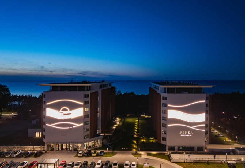 Nowoczesny resort nad morzem z dwoma oświetlonymi budynkami apartamentowymi i dużym parkingiem o zmierzchu