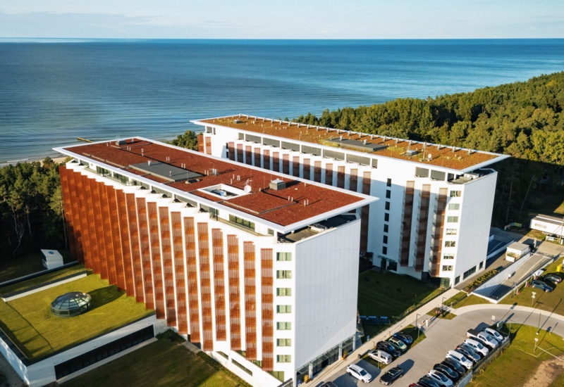 Nowoczesny hotel nad morzem z zielonym dachem i panoramicznym widokiem na plażę oraz otaczający las sosnowy