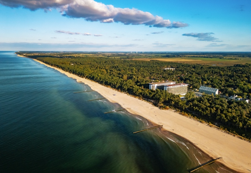 Hotel nad szeroką piaszczystą plażą z widokiem na spokojne morze i otaczający las nadmorski