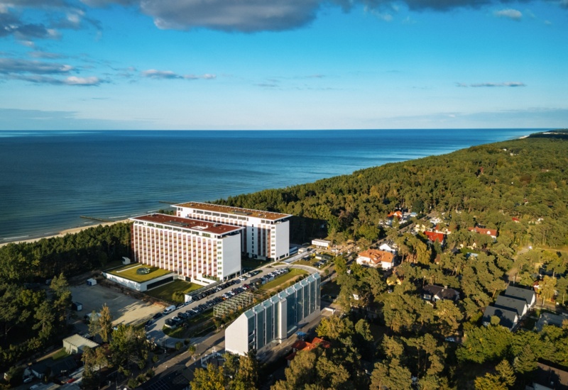 Nowoczesny hotel nadmorski z widokiem na morze i otoczony lasem, z przestronnym parkingiem dla gości.