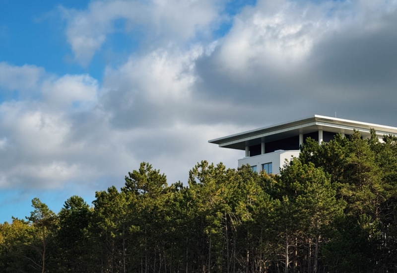 Nowoczesny hotel z tarasem na dachu położony na wzgórzu w otoczeniu zielonego lasu i pod niebem z chmurami