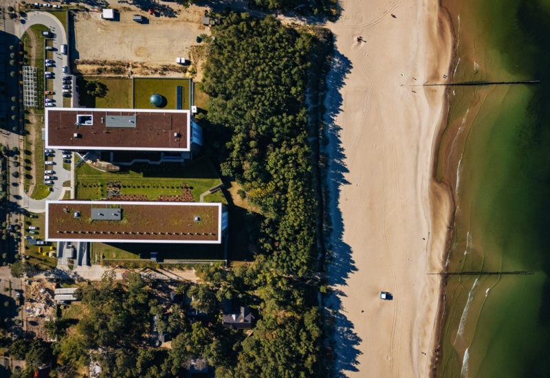 Widok z góry na nowoczesny hotel przy plaży otoczony zielonym lasem i parkingiem, z dostępem do piaszczystego brzegu