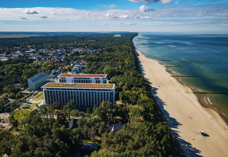 Nowoczesny hotel z balkonami w otoczeniu zieleni przy szerokiej piaszczystej plaży nad spokojnym morzem