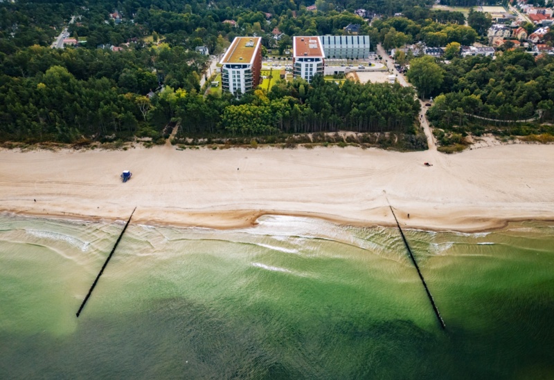 Nadmorski hotel z nowoczesnymi budynkami graniczący z szeroką, piaszczystą plażą i zielonym lasem.