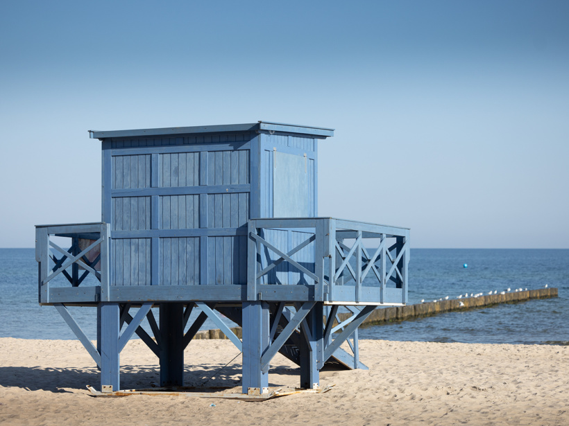 Niebieska drewniana budka ratownika na piaszczystej plaży z widokiem na spokojne morze i drewniany pomost