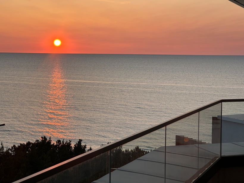 Widok na zachód słońca nad spokojnym morzem z tarasu hotelowego z przezroczystą barierką