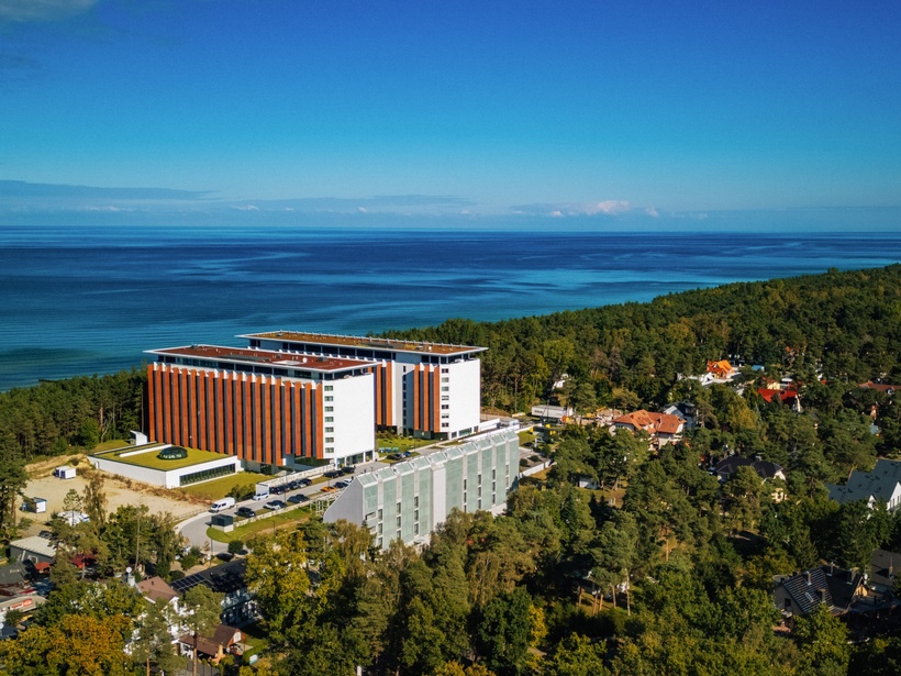 Modernes Hotel mit rot-weißer Fassade am Waldrand, mit Blick auf die ruhige Küste und das blaue Meer.