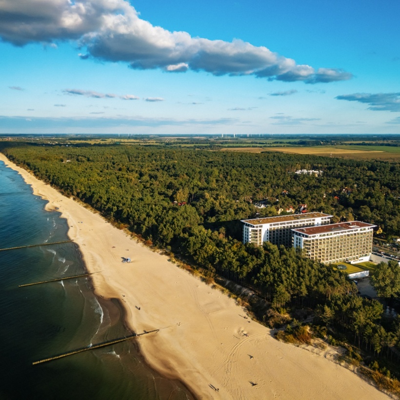 Hotel nad szeroką, piaszczystą plażą z widokiem na morze i otoczony lasem, idealny na wypoczynek nad wodą