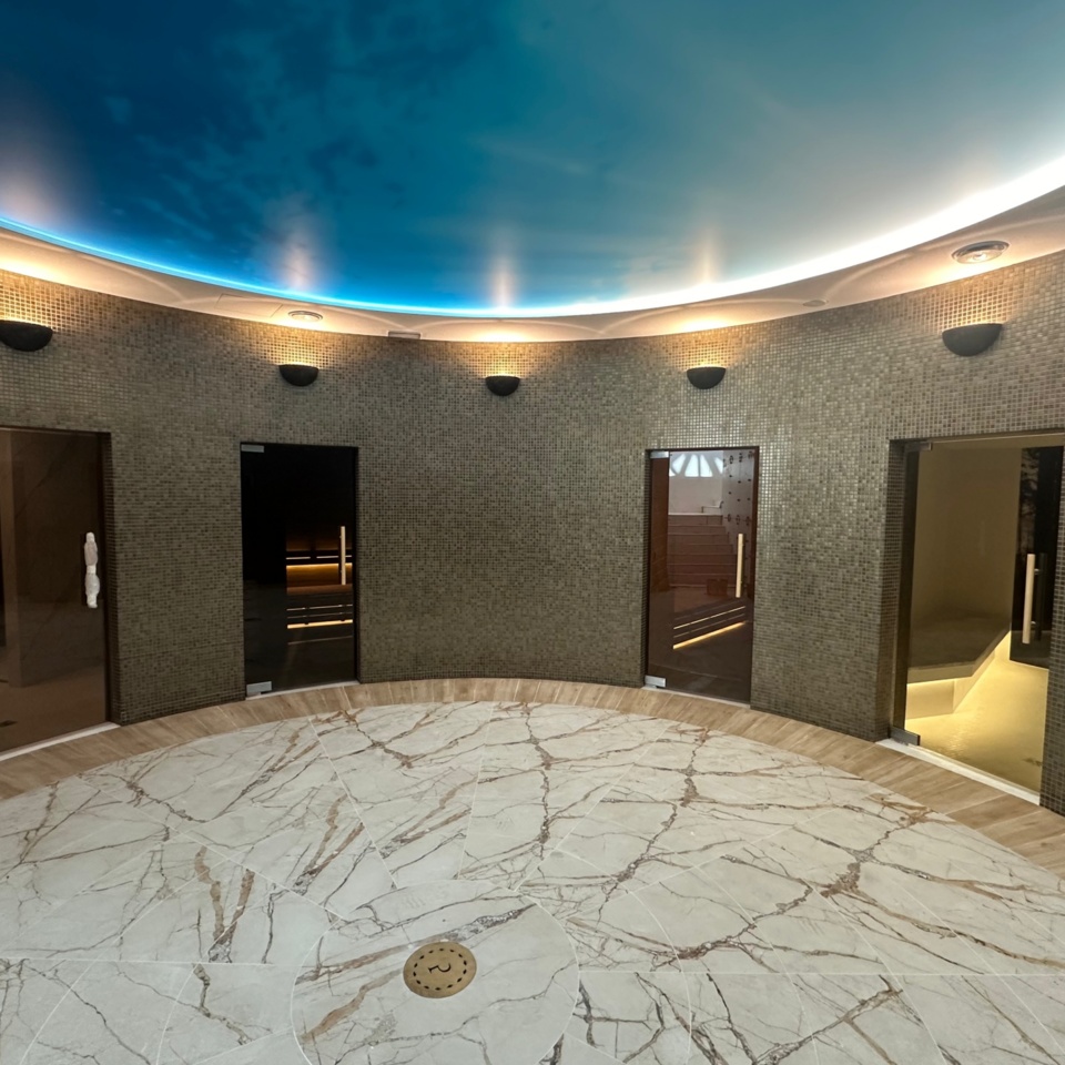 Luksusowa strefa spa z marmurową podłogą, mozaikowymi ścianami i drzwiami do saun oraz gabinetów zabiegowych
