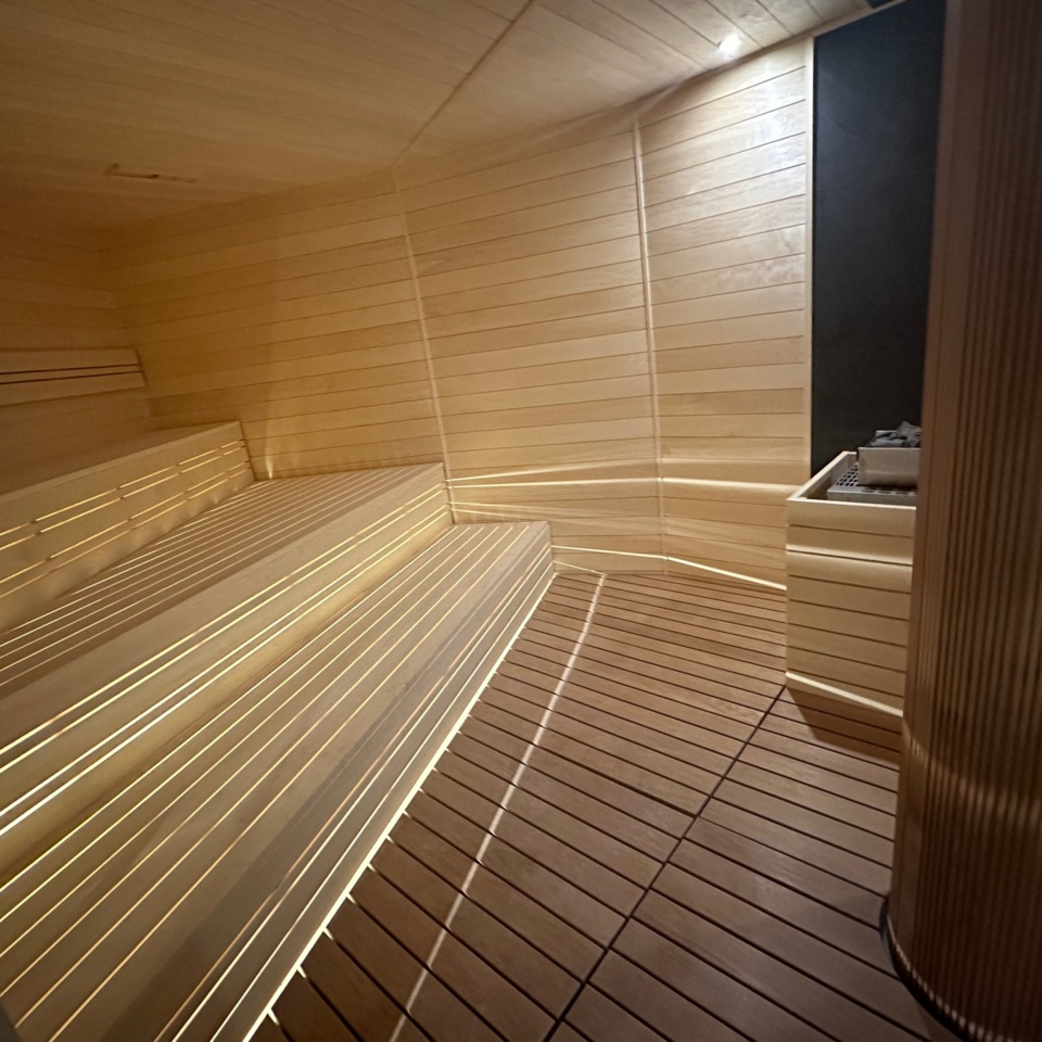 Nowoczesna sauna z jasnym drewnem, wielopoziomowymi ławkami i subtelnym oświetleniem relaksującym gości