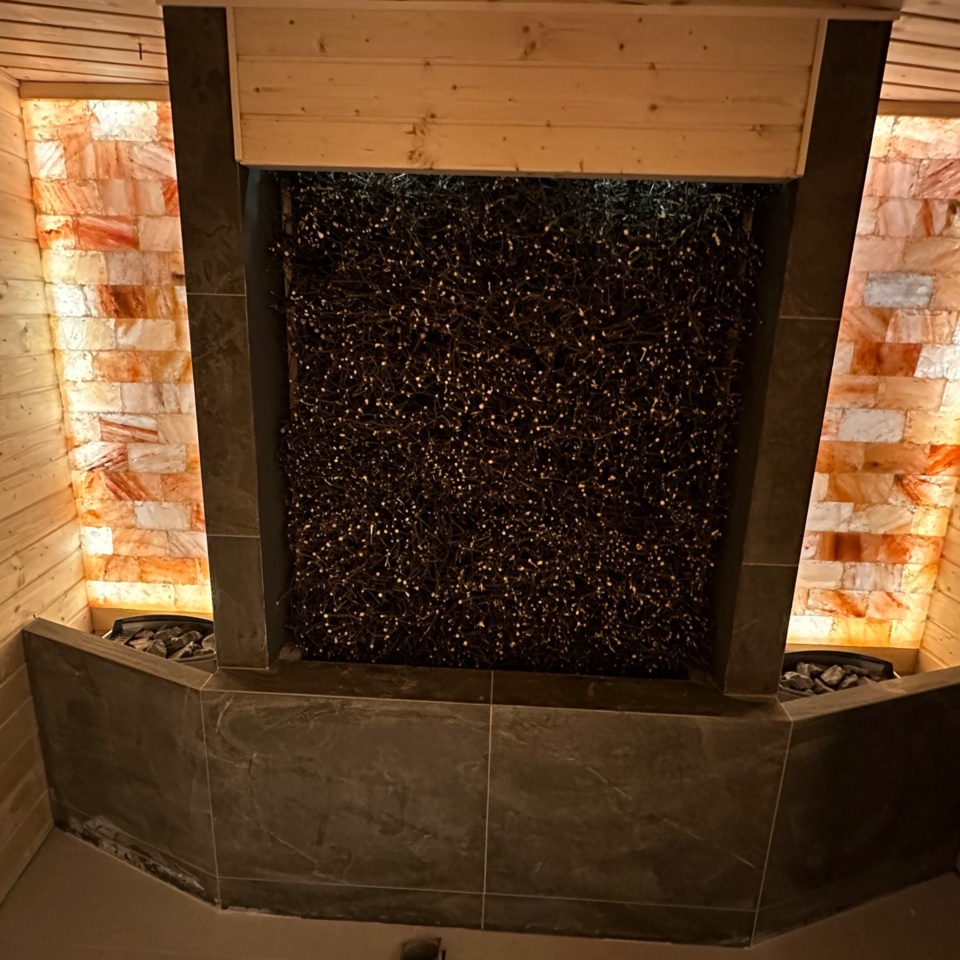 Sauna z drewnianymi panelami i ścianą z podświetlonych płyt soli himalajskiej tworząca relaksującą atmosferę.