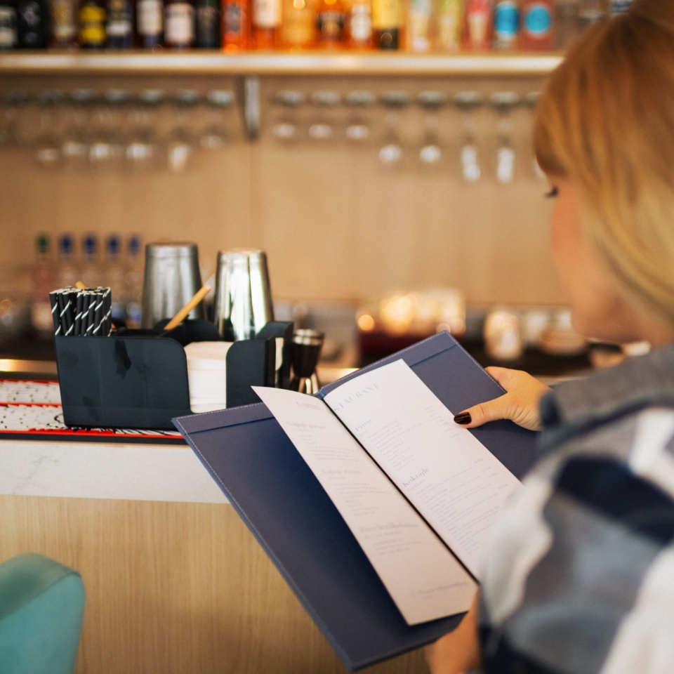 Gośćka przegląda menu w hotelowym barze z nowoczesnym wystrojem i roślinną dekoracją przy ladzie