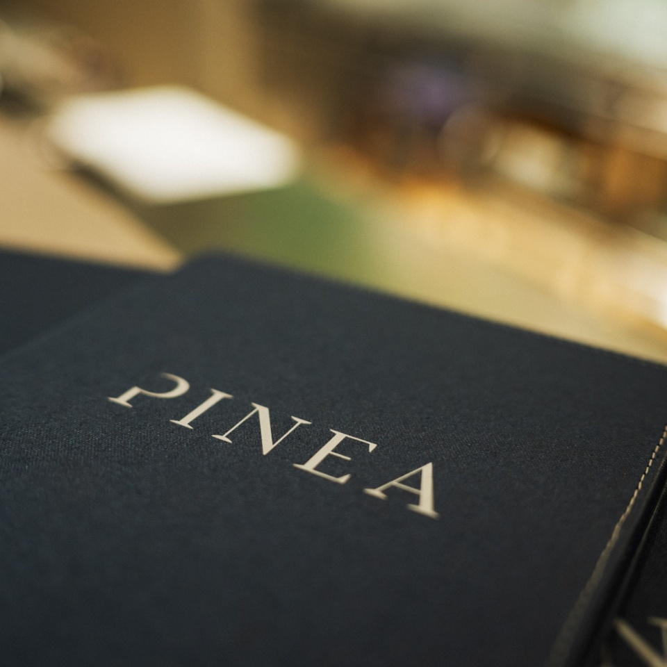 Eleganckie menu restauracji Pinea z granatową okładką na blacie baru.