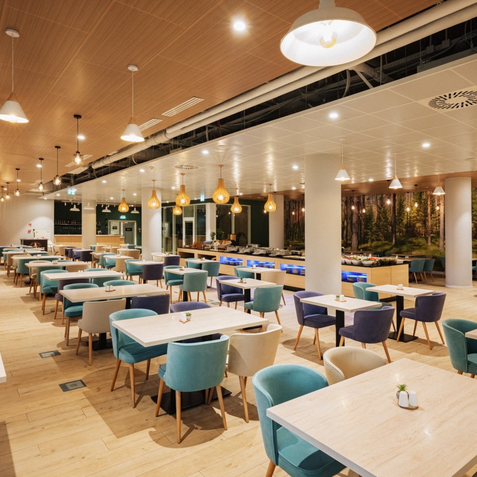 Elegancka restauracja hotelowa z jasnym drewnianym wnętrzem, miękkimi fotelami i bufetem z dekoracjami roślinnymi.