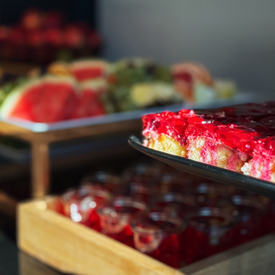 Dezert z czerwoną galaretką podany na czarnej tacy z tacą owoców i deserów w tle