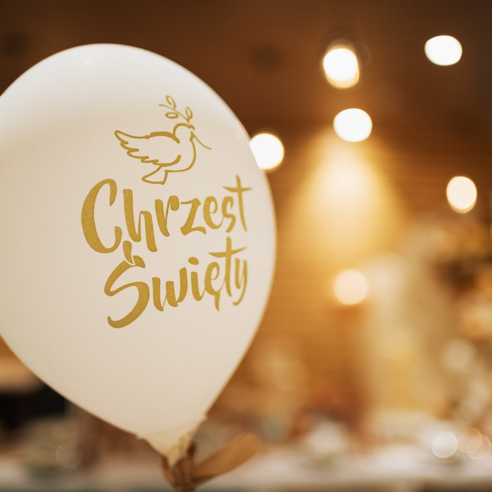 Biały balon z napisem Chrzest Święty i motywem gołębicy, dekoracja przyjęcia w przytulnym, ciepłym wnętrzu