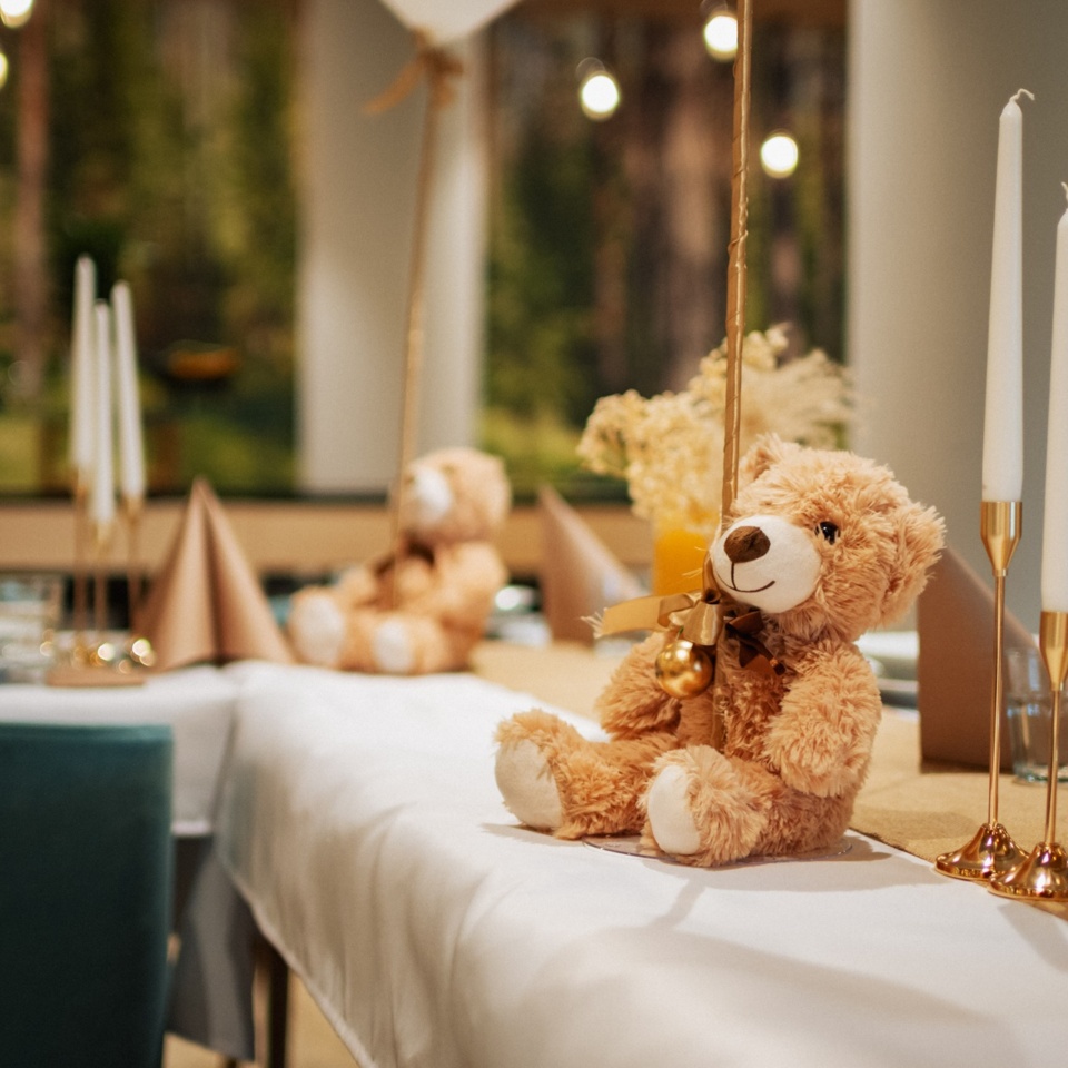 Przytulna dekoracja stołu z pluszowym misiem, białymi świecami i rustykalnymi elementami w eleganckiej jadalni hotelowej