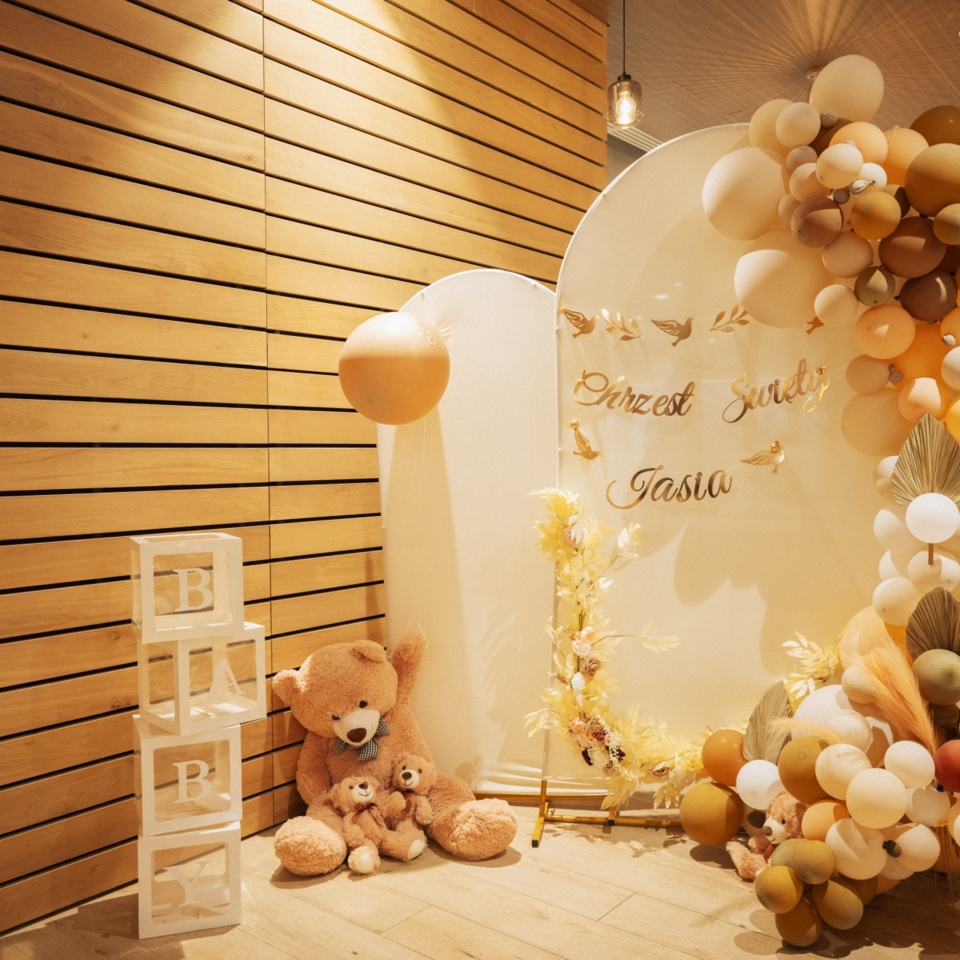 Przytulny kącik dekorowany na chrzciny z brązowymi i beżowymi balonami oraz pluszowymi misiami przy drewnianej ścianie