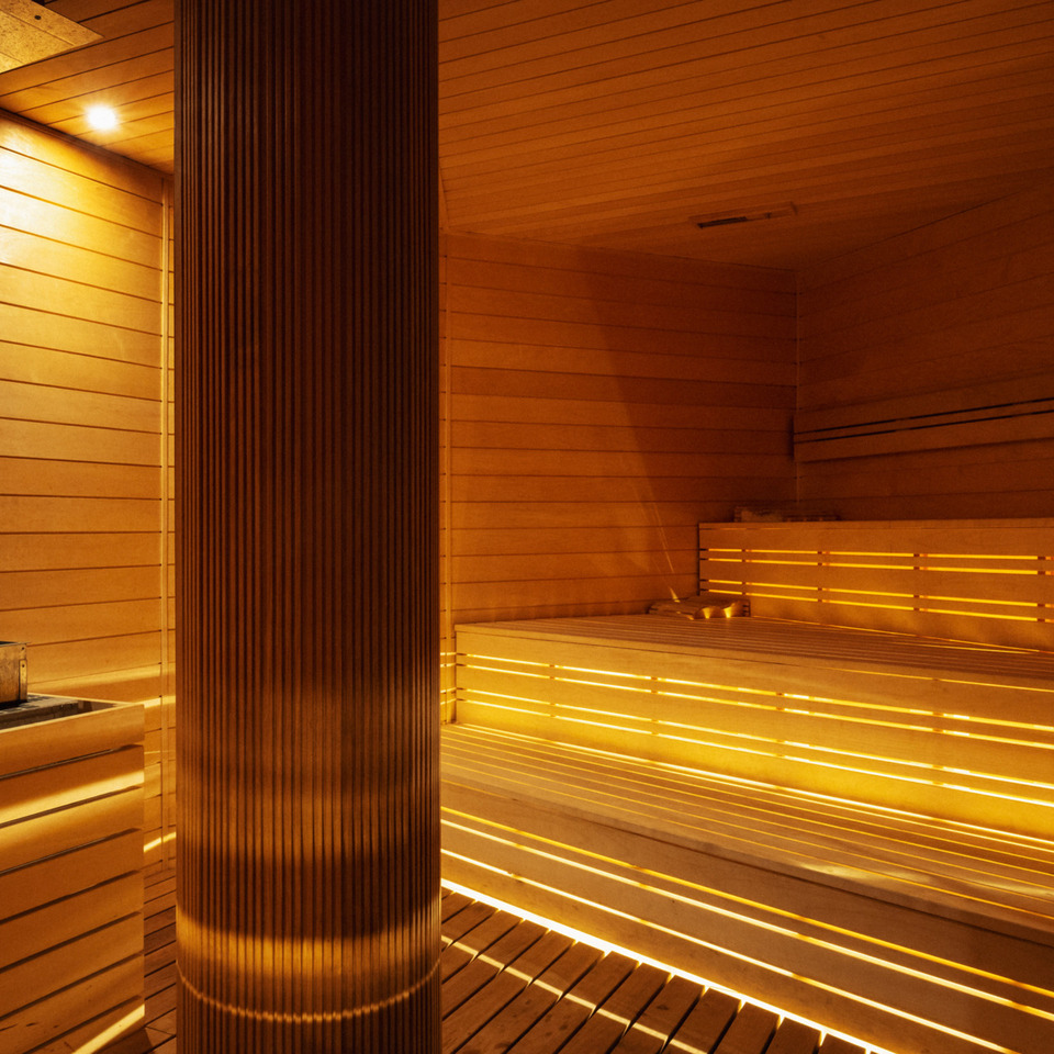 Nowoczesna sauna hotelowa z podświetlanymi drewnianymi ławami i stonowanym, ciepłym oświetleniem relaksacyjnym