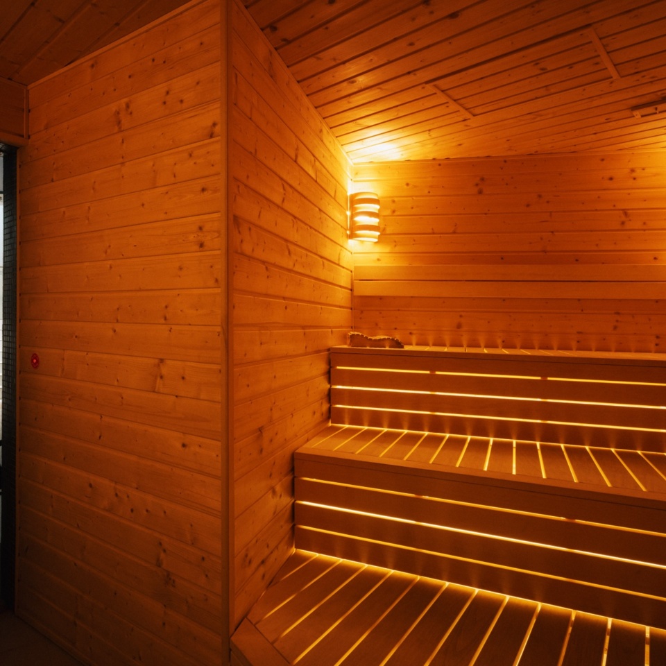 Przytulna sauna hotelowa z drewnianymi ławami podświetlanymi ciepłym światłem i nowoczesnym oświetleniem ściennym.