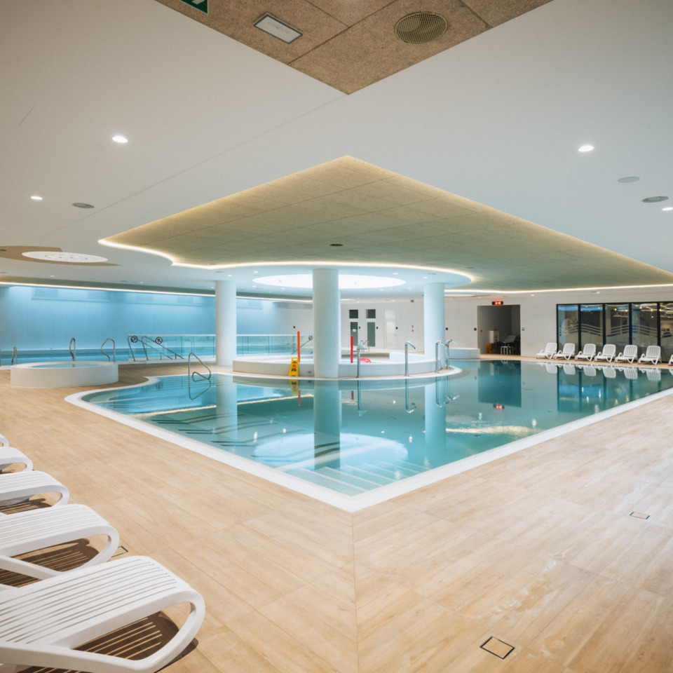 Przestronny, nowoczesny kryty basen hotelowy z leżakami i nastrojowym oświetleniem sufitowym