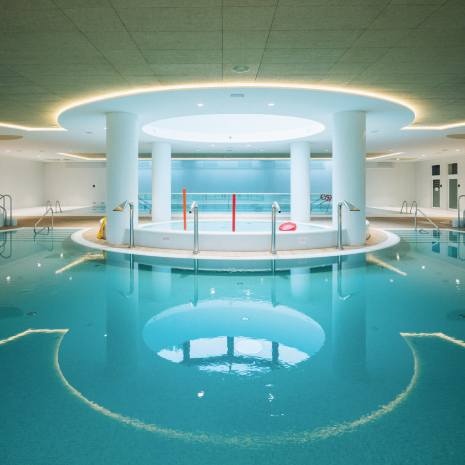 Nowoczesny hotelowy basen wewnętrzny z centralnym jacuzzi, jasnym oświetleniem i minimalistycznym designem