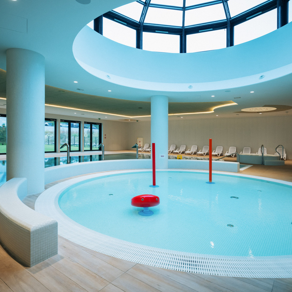 Nowoczesny hotelowy basen kryty z okrągłą niecką dla dzieci i panoramicznym oknem w suficie, leżaki w tle
