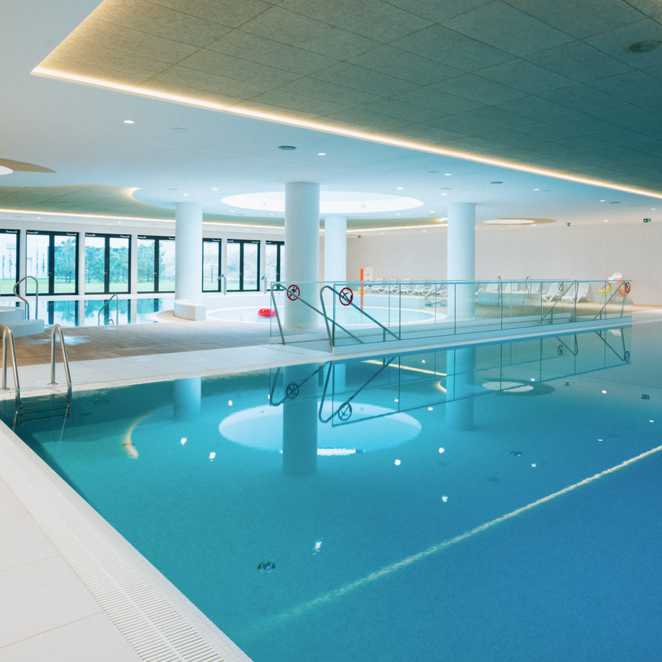 Przestronny, nowoczesny basen kryty z oświetleniem LED i panoramicznymi oknami z widokiem na zieleń na zewnątrz.