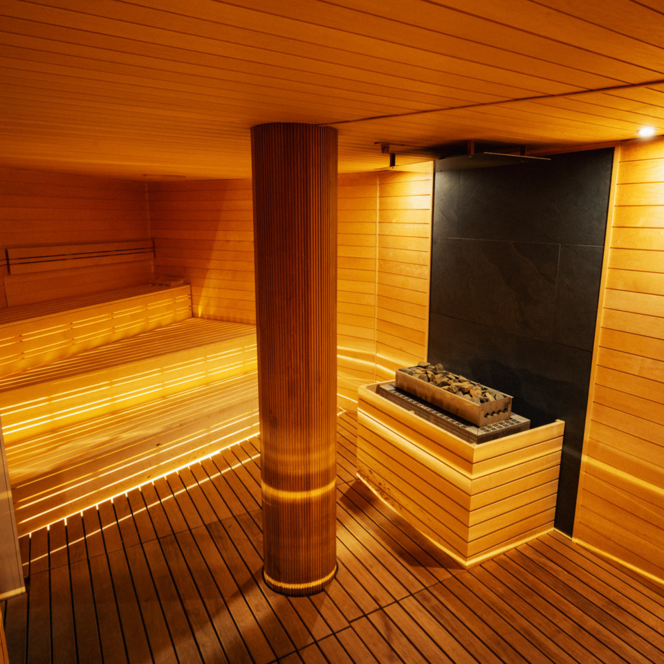 Nowoczesna sauna hotelowa z drewnianymi ławkami, nastrojowym oświetleniem i piecem z kamieniami do sauny.