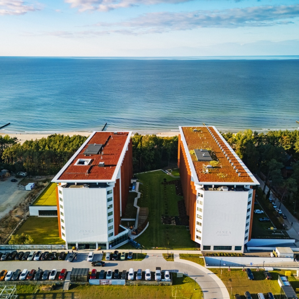 Nowoczesny hotel nadmorski z dwoma blokami, zielonym patio i widokiem na plażę i morze z lasem sosnowym w tle