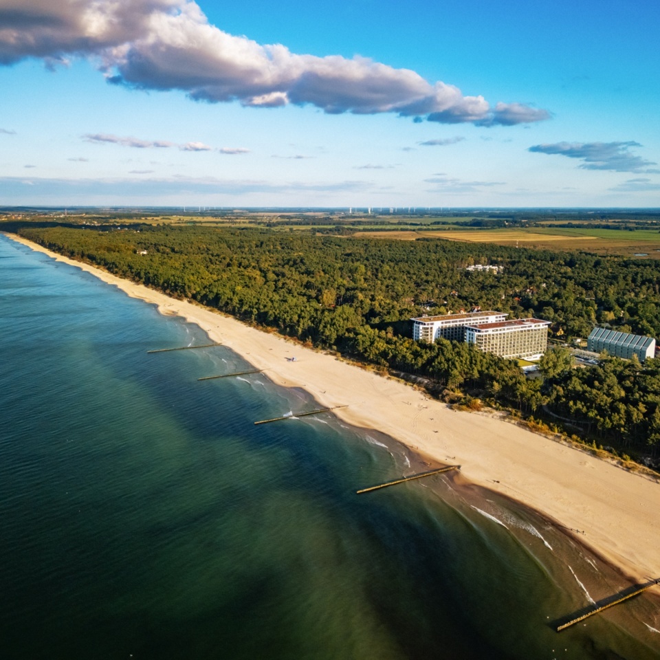 Hotel nad szeroką piaszczystą plażą z widokiem na spokojne morze i otaczający las nadmorski