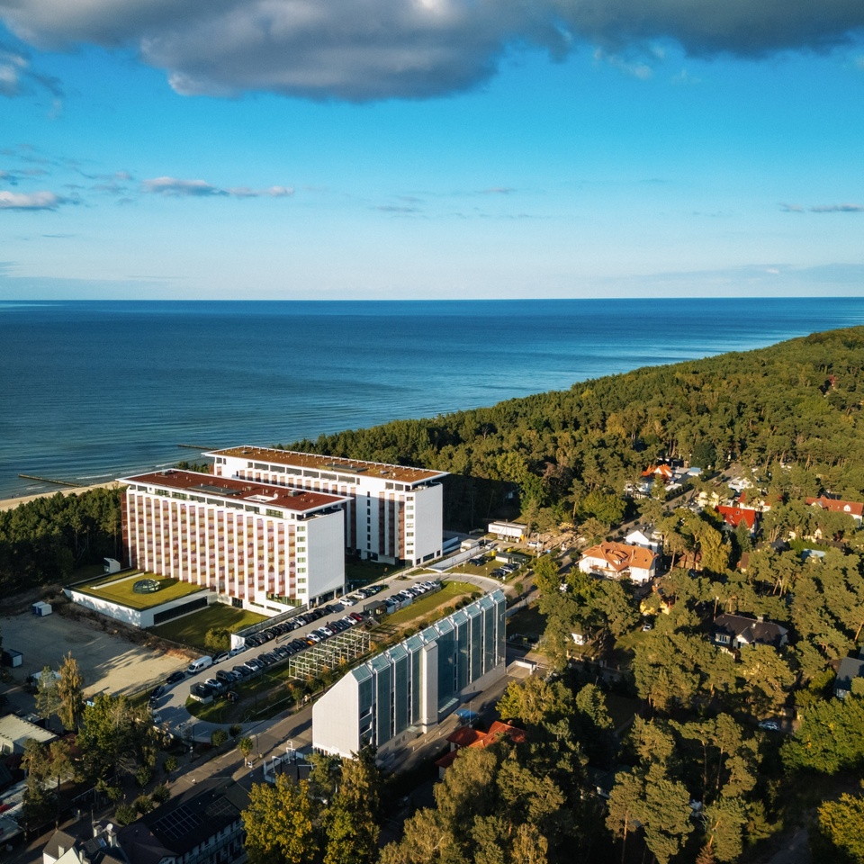 Hôtel moderne en bord de mer avec vue sur l'océan, entouré de forêt, disposant d'un grand parking pour les clients.
