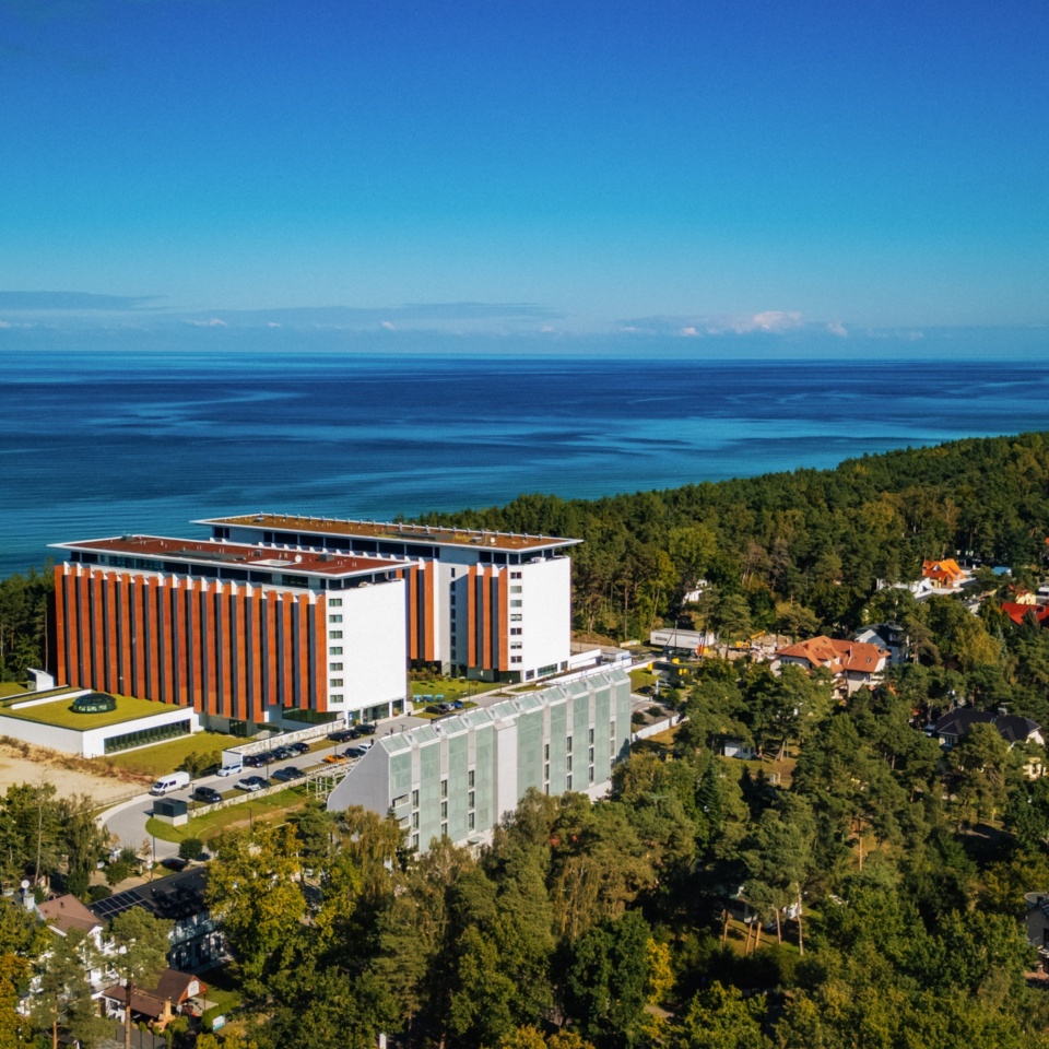 Nowoczesny hotel z czerwono-białą elewacją przy lesie, z widokiem na spokojne wybrzeże i morze.