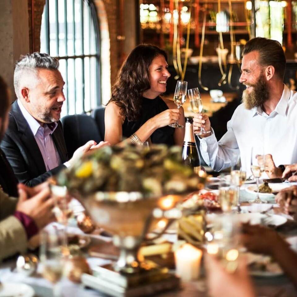Guests toast with champagne over a candlelit seafood platter in an elegant brick‑walled restaurant with arched windows