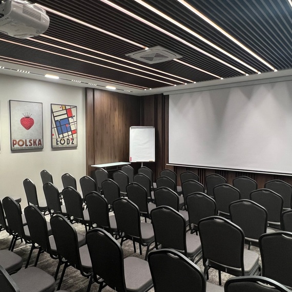 Nowoczesna sala konferencyjna z rzędem szarych krzeseł, dużym ekranem projekcyjnym i rzutnikiem, idealna na spotkania biznesowe.