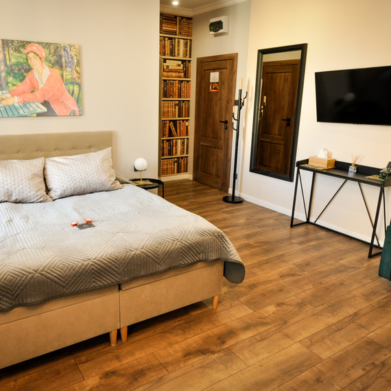 Cozy hotel room with a double bed, a decorative painting on the wall, a large mirror and a wall-mounted television.