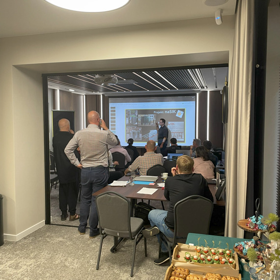 Conference room with participants during a presentation, with a buffet of snacks and drinks in the foreground.