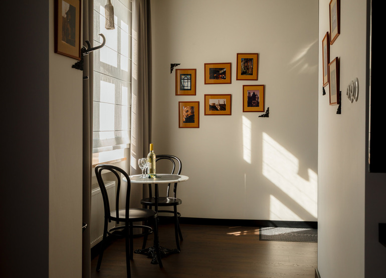 Przytulny kącik z okrągłym stołem, dwoma czarnymi krzesłami, butelką wina i dwoma kieliszkami w jasnym pokoju hotelowym