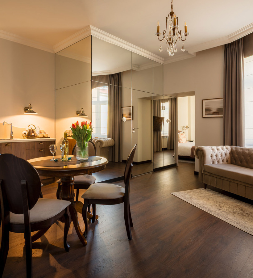 Elegancki apartament z jadalnią, kuchnią, beżową sofą, kryształowym żyrandolem i dużą szafą z lustrzanymi drzwiami.