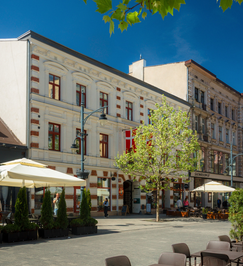Cozy café on a pedestrian street with umbrellas and greenery, surrounded by historic townhouses with ornate façades.
