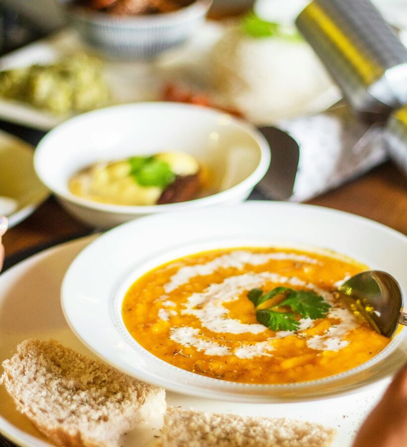 Creamy squash soup with cream swirl and parsley in a white bowl, served with sliced crusty bread