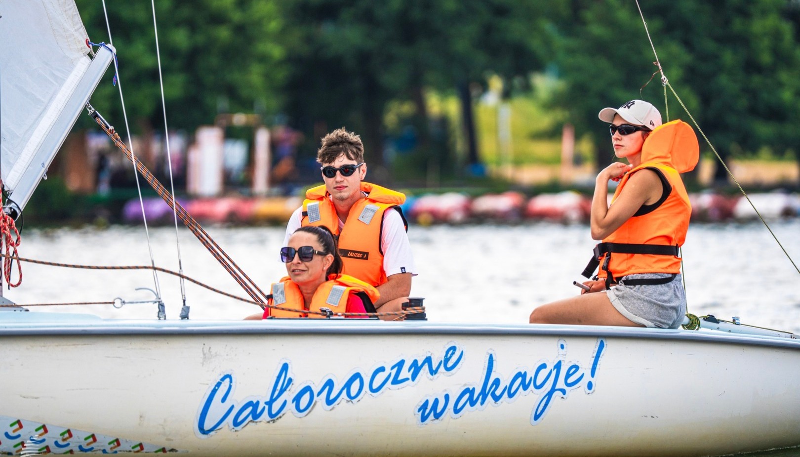 Trzy osoby w pomarańczowych kamizelkach na żaglówce, relaks podczas rejsu po jeziorze