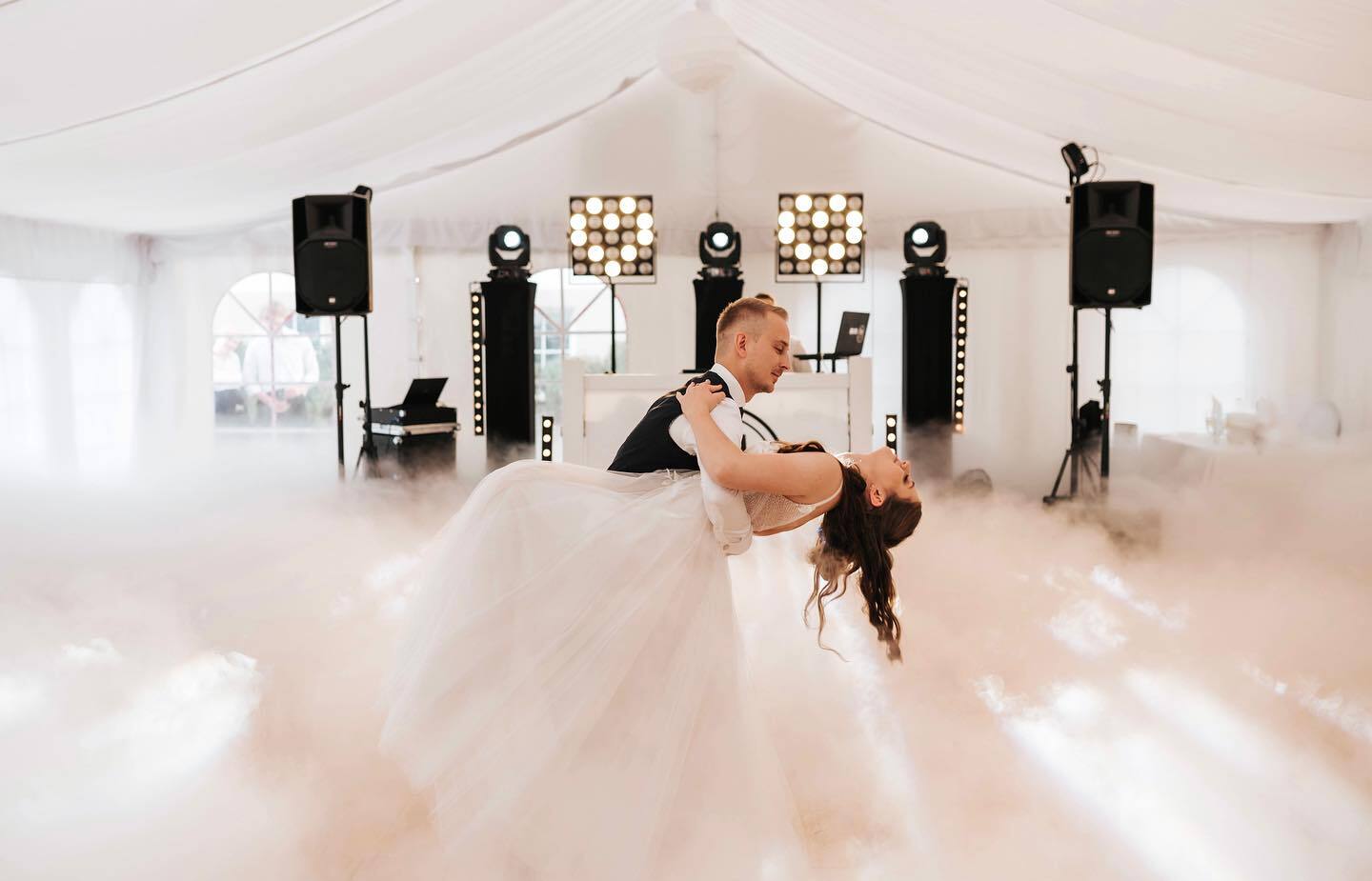 Para młoda podczas romantycznego pierwszego tańca w eleganckim namiocie z niską mgiełką, stanowiskiem DJ i scenicznym oświetleniem.