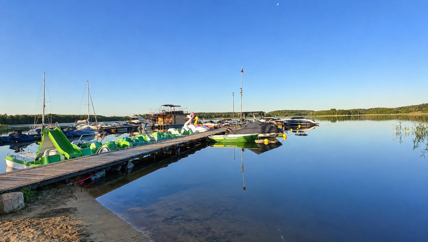 Seemarina mit bunten Tretbooten und Schwan-Luftbooten am Holzsteg, ruhiges Wasser und sandiges Ufer