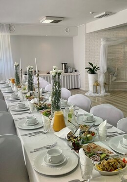 White banquet room with long set table, tall floral centerpieces, plated salads and juice, sheer curtains and canopy swing