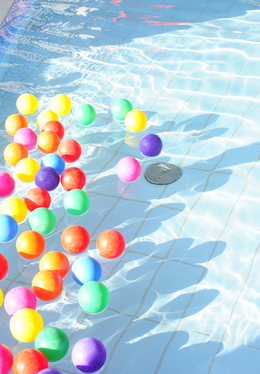 Shallow hotel pool with colorful floating play balls, tiled edge and bright sunlit water ideal for families