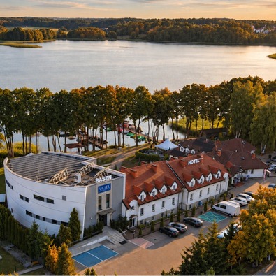 Seehotel mit roten Ziegeldächern, modernem Schwimmbadgebäude, Steg, Baumreihe und malerischem Seeblick bei Abendlicht