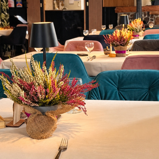 Przytulna restauracja hotelowa z turkusowymi i różowymi aksamitnymi krzesłami, obrusami, sezonowymi bukietami i stołowymi lampami