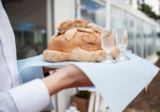 Dekoratives rundes Brot mit geflochtenem Rand und Teigblumen, auf Tablett serviert mit zwei Gläsern prickelndem Getränk.