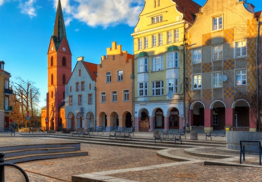 Historischer Marktplatz mit Kopfsteinpflaster, bunten Giebelhäusern, Arkaden und rotem Backstein-Kirchturm
